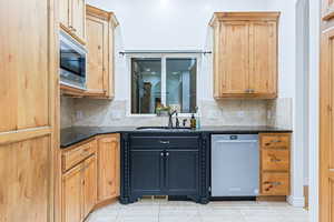 Kitchen with dark stone counters, sink, light tile patterned floors, and stainless steel appliances