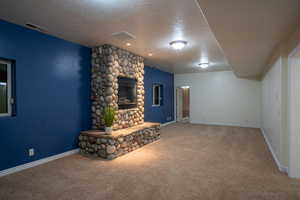 Unfurnished living room with carpet, a textured ceiling, and a stone fireplace