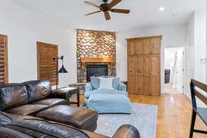 Living room with light hardwood / wood-style flooring, ceiling fan, and a stone fireplace