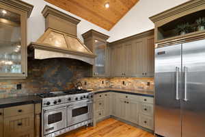 Kitchen featuring custom exhaust hood, tasteful backsplash, premium appliances, vaulted ceiling, and light hardwood / wood-style floors