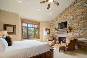 Carpeted bedroom featuring a fireplace, ceiling fan, and high vaulted ceiling