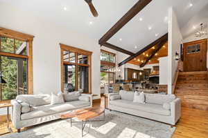 Living room featuring ceiling fan with notable chandelier, light hardwood / wood-style floors, beam ceiling, and high vaulted ceiling