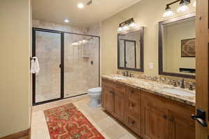 Bathroom featuring tile patterned flooring, vanity, toilet, and a shower with door