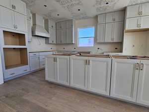 Kitchen featuring white cabinets, a textured ceiling, light hardwood / wood-style flooring, and custom range hood