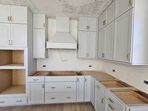 Kitchen featuring white cabinets, custom exhaust hood, light hardwood / wood-style floors, and a textured ceiling