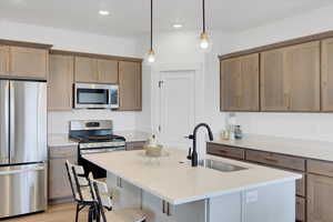 Kitchen featuring sink, appliances with stainless steel finishes, a kitchen breakfast bar, an island with sink, and hanging light fixtures