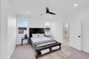 Carpeted bedroom with ensuite bathroom, multiple windows, and ceiling fan