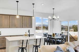 Kitchen with light wood-type flooring, a notable chandelier, pendant lighting, sink, and a kitchen island with sink