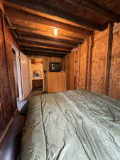 Unfurnished bedroom featuring wooden walls and beam ceiling