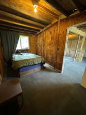 Unfurnished bedroom featuring wooden walls, beam ceiling, and carpet