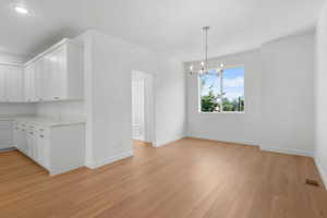 Kitchen with pendant lighting, an inviting chandelier, light hardwood / wood-style flooring, and white cabinetry