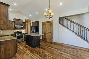 Kitchen with light stone counters, a kitchen island, a chandelier, stainless steel appliances, and dark hardwood / wood-style flooring