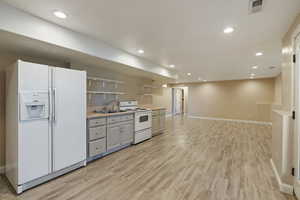 Kitchen with white cabinets, white appliances, light hardwood / wood-style floors, and sink