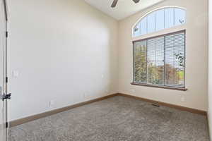 Carpeted spare room featuring ceiling fan and high vaulted ceiling