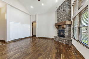 Unfurnished living room with dark hardwood / wood-style flooring, ceiling fan, high vaulted ceiling, and a stone fireplace