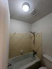 Bathroom featuring a textured ceiling, toilet, and shower / bathing tub combination