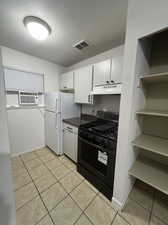 Kitchen with white cabinets, light tile patterned floors, white fridge, a textured ceiling, and black range with gas cooktop