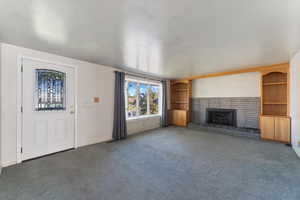 Large living room featuring a brick fireplace with electric insert and dark carpet