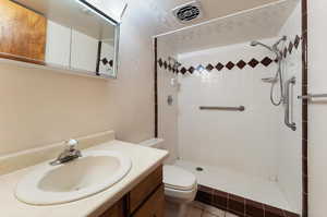 Basement bathroom featuring a tile shower, vanity, toilet, and tile patterned floors