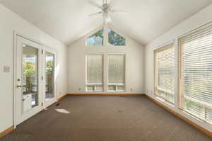 Carpeted spare room with vaulted ceiling, ceiling fan, and plenty of natural light