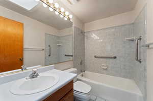 Main floor full bathroom with a skylight, tile patterned floors, vanity, tiled shower / bath, and toilet