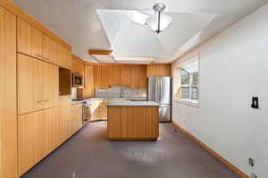 Kitchen with a textured ceiling, sink, a kitchen island, stainless steel appliances, and a skylight