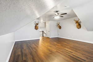 Bonus room with a textured ceiling, vaulted ceiling, ceiling fan, and dark wood-type flooring