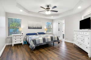 Bedroom featuring connected bathroom, a tray ceiling, ceiling fan, and dark wood-type flooring