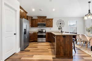 Kitchen featuring a kitchen breakfast bar, stainless steel appliances, light hardwood / wood-style flooring, decorative light fixtures, and sink