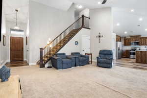 Carpeted living room featuring ceiling fan with notable chandelier and high vaulted ceiling