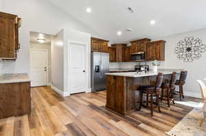 Kitchen with light stone counters, appliances with stainless steel finishes, light hardwood / wood-style floors, and kitchen peninsula