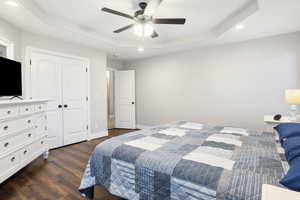 Bedroom featuring a raised ceiling, dark hardwood / wood-style flooring, ceiling fan, and a closet