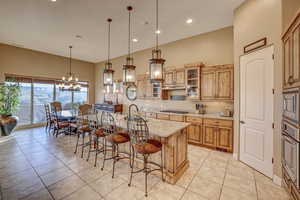 Kitchen with a chandelier, a kitchen island with sink, light tile patterned flooring, a kitchen bar, and appliances with stainless steel finishes