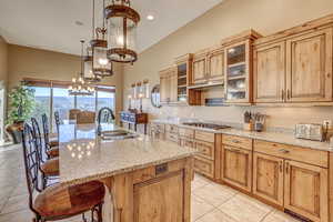 Kitchen with an island with sink, sink, stainless steel gas cooktop, a chandelier, and a breakfast bar