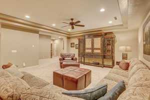 Living room featuring light carpet, a tray ceiling, and ceiling fan