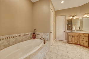 Bathroom featuring tiled tub, vanity, and tile patterned floors