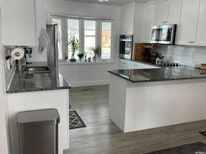 Kitchen featuring sink, white cabinetry, kitchen peninsula, stainless steel appliances, and dark stone countertops