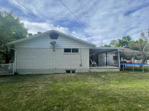 Back of property featuring a trampoline and a yard