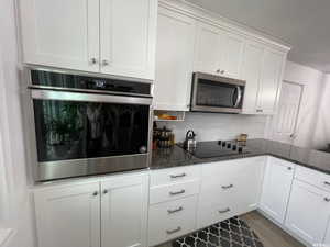 Kitchen featuring stainless steel appliances, white cabinets, and dark stone countertops