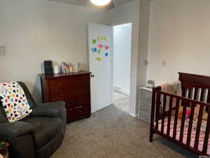 Bedroom featuring light carpet, ceiling fan, and a nursery area