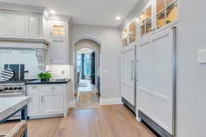 Kitchen with stainless steel stove, light hardwood / wood-style floors, decorative backsplash, and white cabinetry