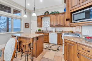 Kitchen featuring a center island, stove, stainless steel microwave, ornamental molding, and white dishwasher