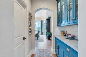 Bar with light stone counters, tasteful backsplash, light hardwood / wood-style flooring, ornamental molding, and blue cabinets