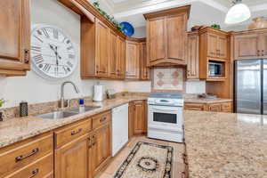 Kitchen with sink, hanging light fixtures, appliances with stainless steel finishes, light tile patterned floors, and light stone countertops