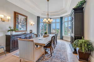 Dining space with ornamental molding, a notable chandelier, a tray ceiling, and light hardwood / wood-style floors