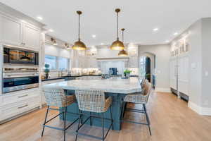 Kitchen featuring white cabinets, pendant lighting, stainless steel appliances, light wood-type flooring, and a kitchen bar