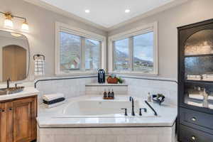 Bathroom featuring a relaxing tiled tub, vanity, and ornamental molding