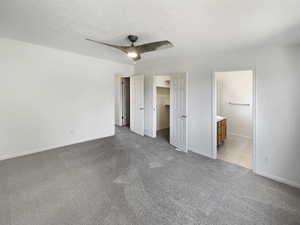 Unfurnished bedroom featuring a spacious closet, ceiling fan, ensuite bathroom, and a textured ceiling