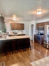 Kitchen with a breakfast bar, wood-type flooring, a textured ceiling, and appliances with stainless steel finishes