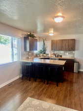 Kitchen with a textured ceiling, kitchen peninsula, dark hardwood / wood-style flooring, and a kitchen bar